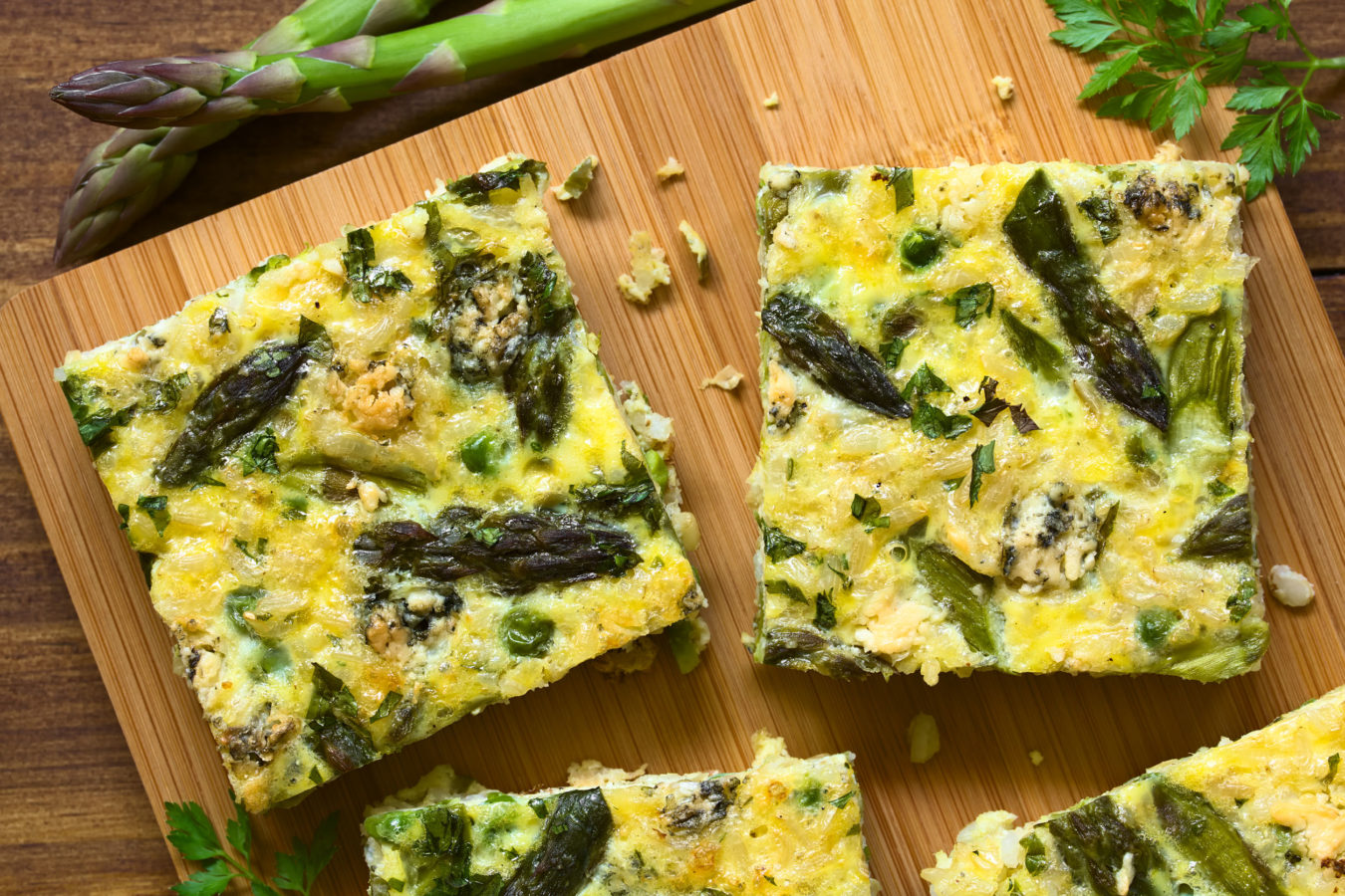 Frittata made of eggs, green asparagus, pea, blue cheese, parsley and brown rice, photographed overhead on wooden board with natural light