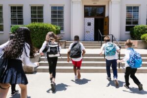 Group of children wearing backpacks running up the front of a school building