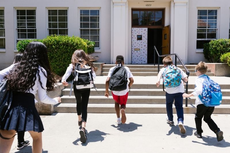 Group of children wearing backpacks running up the front of a school building