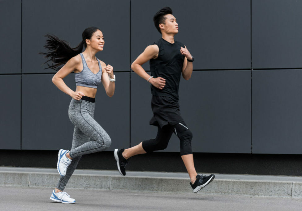 side view of asian sportsman and sportswoman running at city street